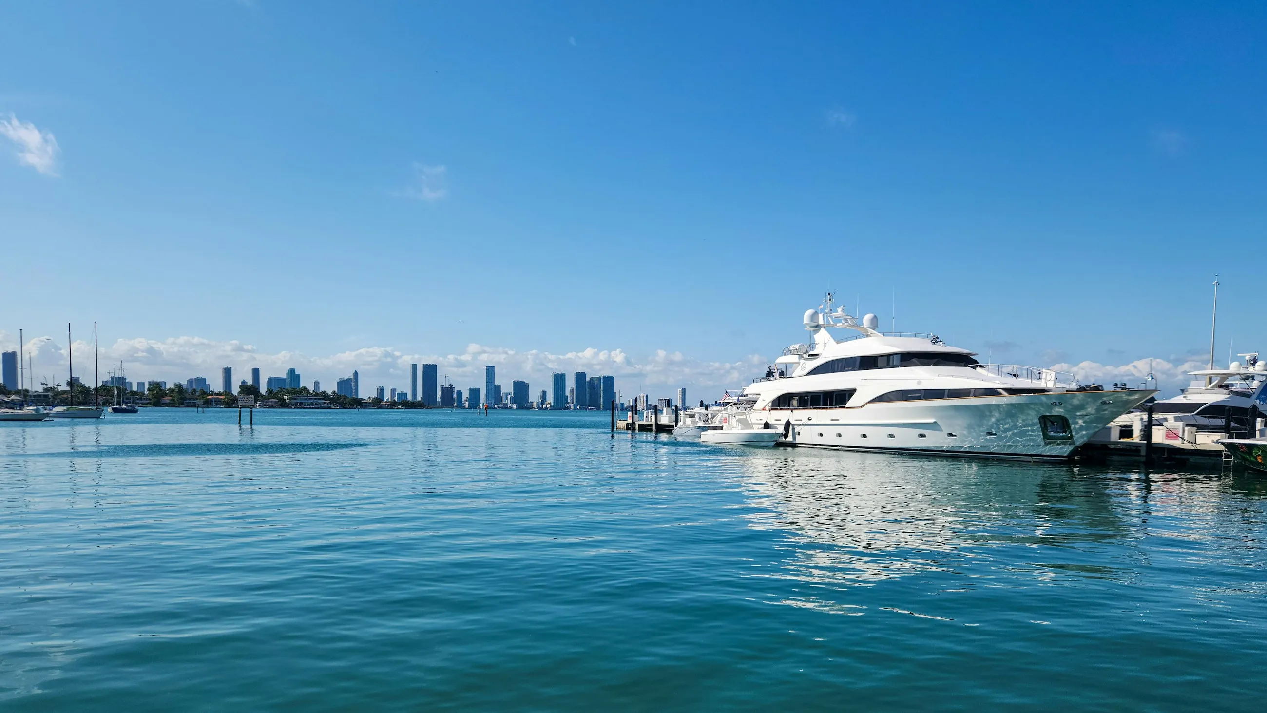 Un yate de lujo blanco amarrado en aguas turquesa y tranquilas, con el horizonte de Miami al fondo