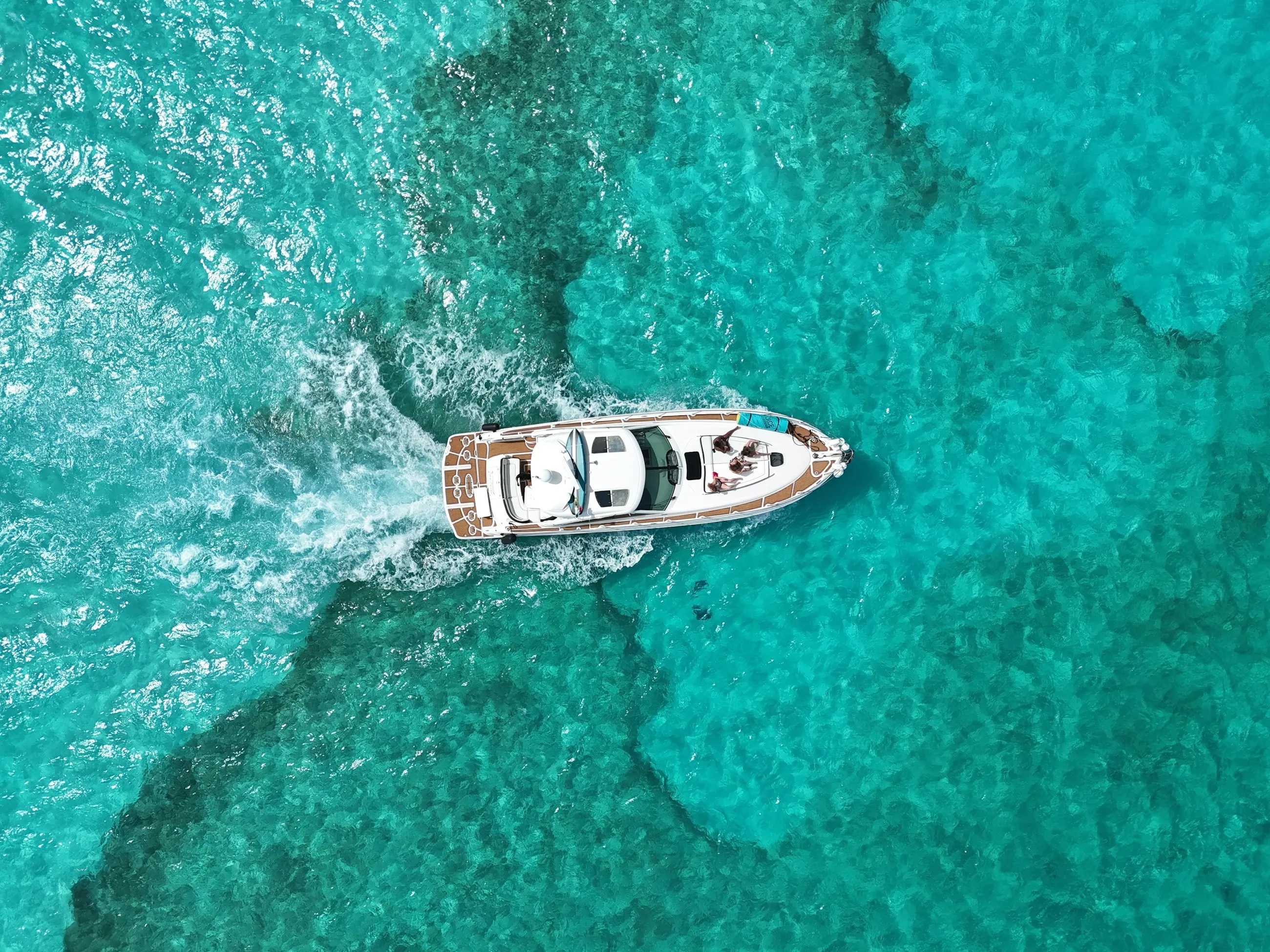 A yacht cruising over turquoise water, seen from above