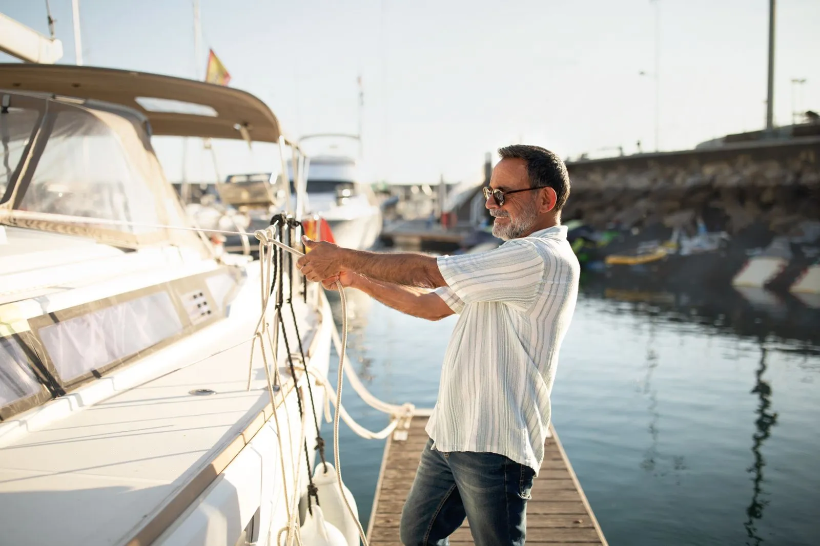 Un hombre con gafas de sol amarrando un barco al muelle de una marina